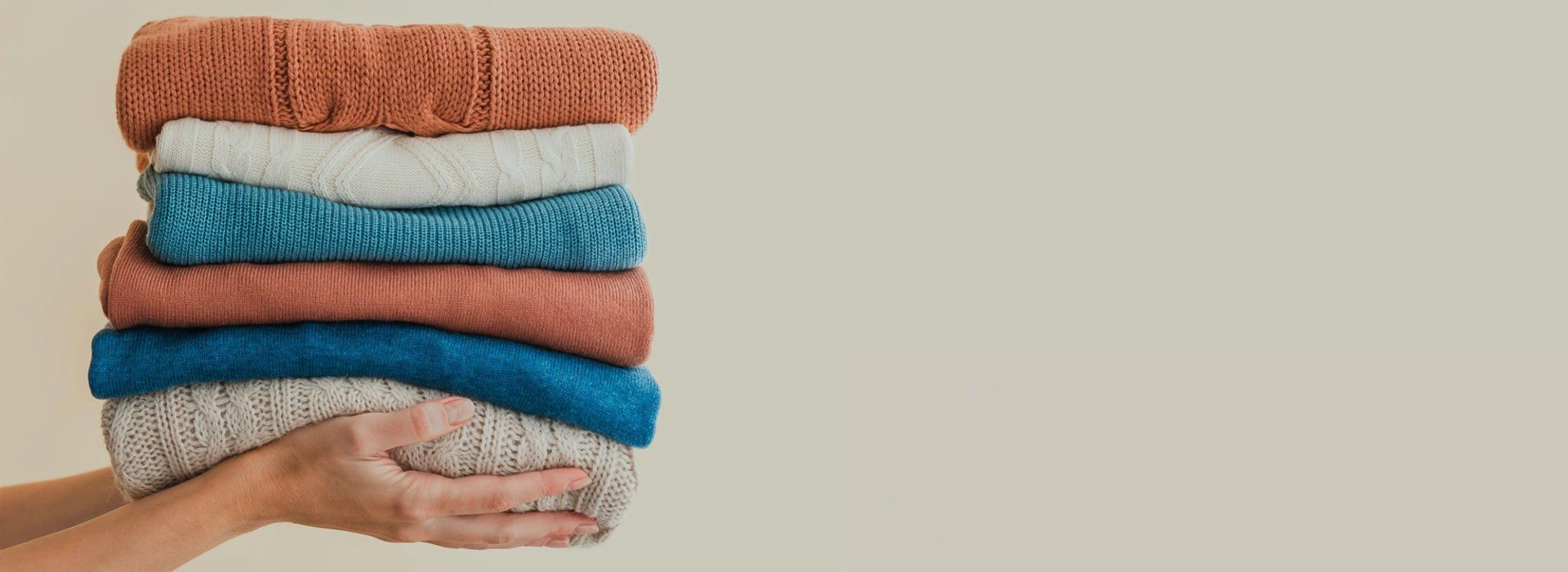 a person holding folded different types of sweater