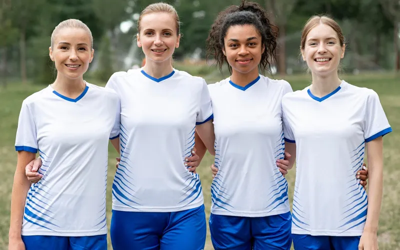 A group of children posing in matching white soccer uniforms with blue accents, smiling and standing outdoor