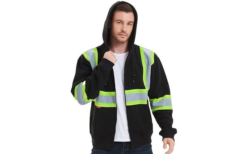 A man wearing a black hoodie with bright reflective stripes across the chest and shoulders, featuring a zipper and a hood, standing confidently outdoors.