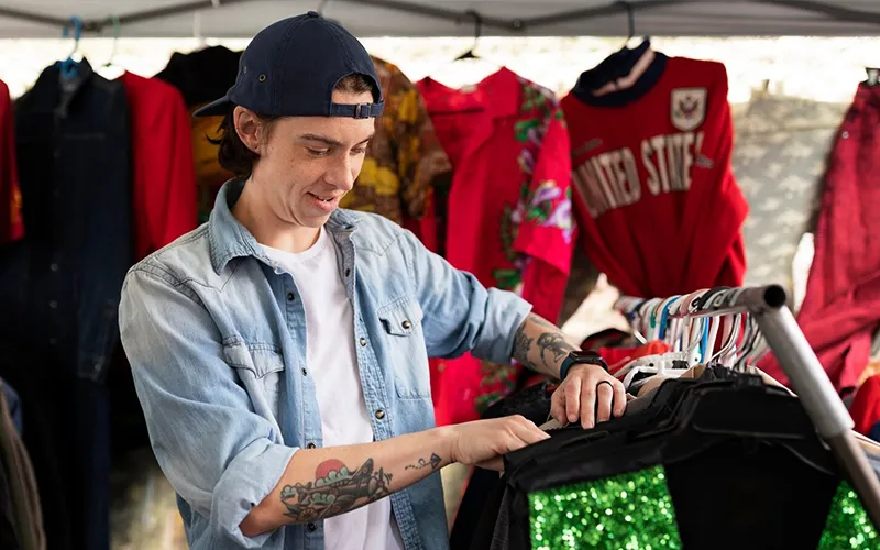 A man shopping for jersey in a custom sportswear store, inspecting white shirts on a rack while wearing a name badge