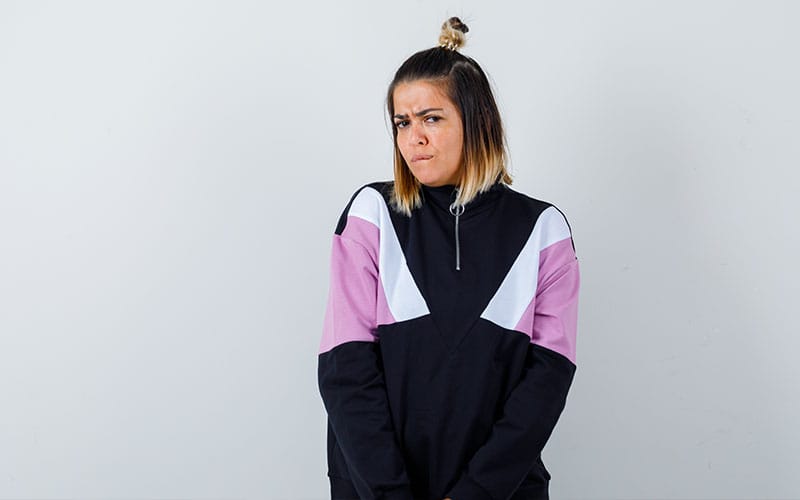 Young woman wearing a half-zip sweatshirt with pink and black color blocks, making a thoughtful expression against a plain white background.