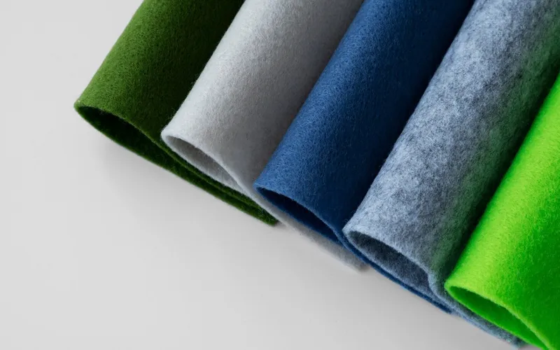 Close-up view of rolled fabric pieces in different colors, including shades of green, gray, and blue, displayed on a white surface.